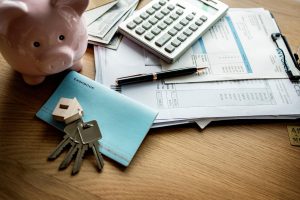 Piggy bank, calculator, keys, and financial documents on a desk representing property costs and lien-related due diligence.